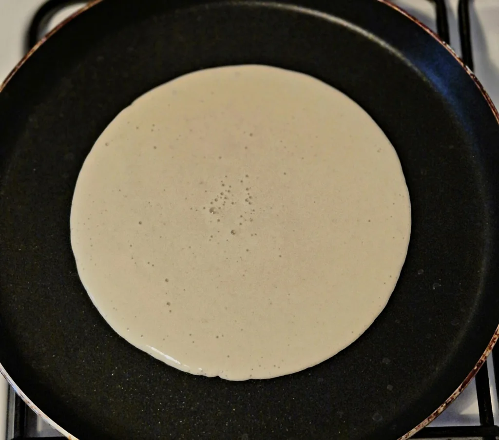 A single Moroccan  pancake "Beghrir" batter circle in a nonstick skillet, beginning to bubble around the edges.